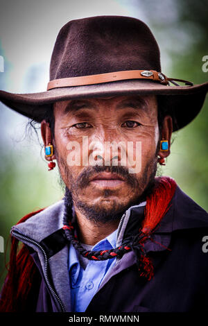 Lhasa, Tibet. Juli 2016 20. Nahaufnahme Porträt einer ethnischen Mann mit Türkis Ohrringe und einen Hut. Foto: Bryan Watt Stockfoto