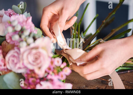 Junge weibliche Hände binden von Knoten und Bug, während zur Festsetzung beige Seidenband um florale Bündel Stockfoto