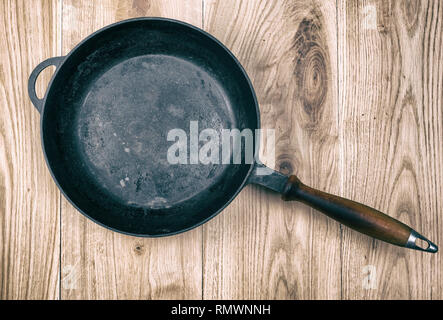 Leere schwarze runde Pfanne mit Holz- auf einen hölzernen Tisch Griff, Ansicht von oben Stockfoto