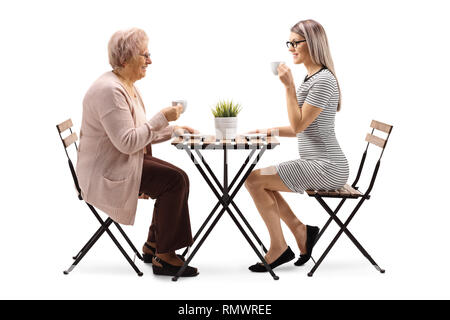 Volle Länge Profil Schuß einer älteren Frau trinkt Kaffee mit einer jungen Frau an einem Tisch auf weißem Hintergrund Stockfoto