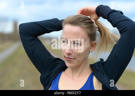 Attraktive junge Frau, die Band ihre langen blonden Haare wie Sie sich vorbereitet, joggen auf dem Land in der Nähe zu Kopf und Schultern portrait Stockfoto