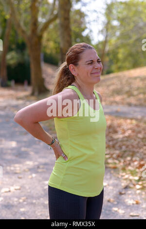 Frau mittleren Alters Joggen erleidet eine Muskelverletzung Rücken hielt sie senken und Grimassen in den Schmerz, in der Nähe der oberen Körper anzeigen Stockfoto