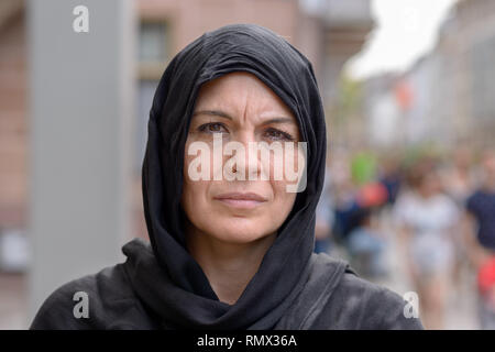 Ernsthafte Frau mittleren Alters, der ein schwarzes Kopftuch oder Hijab in Nahaufnahme Kopf geschossen in einer belebten Straße Stockfoto