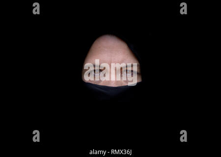 Studio shot Porträt einer muslimischen Frau mittleren Alters auf Kamera mit ernsten Augen Ausdruck beim Tragen schwarze Hijab auf schwarzem Hintergrund f Stockfoto