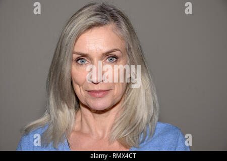 Attraktive blue-eyed blonde Frau mittleren Alters mit einem süßen Lächeln und schulterlanges Haar an Kamera suchen Stockfoto