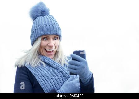 Lachend lebendig trendige Frau in Blau winter fashion mit Handy in Ihren behandschuhten Hand auf Weiß mit Kopie Raum isoliert Stockfoto