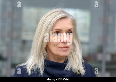 Ziemlich nachdenklich blue eyed blonde Frau aus auf der rechten Seite der Linse mit einem verträumten fernen Ausdruck über einen grauen städtischen Hintergrund starren Stockfoto