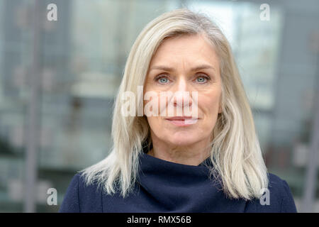 Attraktive blonde Frau mit blauen Augen in einer städtischen Straße posiert an der Kamera, die mit einem ruhigen Lächeln Stockfoto