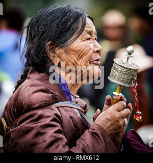 Lhasa, Tibet. Juli 2016 20. Nahaufnahme Porträt einer ethnischen Frau in traditioneller Kleidung beten mit dem Handheld Gebetsmühle. Foto: Bryan Wa Stockfoto