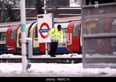 Bild zeigt: Schnee und Schneeregen behindert Pendler auf ihre Arbeit heute im East Finchley, London Mann Clearing Plattform an der tube station pic von Stockfoto