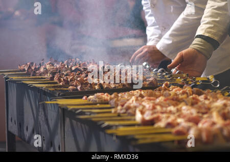 Der Küchenchef bereitet Barbecue auf dem Grill. Traditionelle kaukasische Teller auf Feuer gekocht. Der Koch dreht das Fleisch am Spieß. Stockfoto