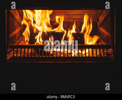 Brennholz brennt im Kamin mit einer hellen Flamme hinter verschlossenen Glastür Stockfoto
