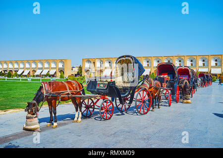 Die Warteschlange der touristische Kutschen in der Mitte Naqsh-e Jahan Platz mit Säulengang og Grand (soltani) Basar auf dem Hintergrund, Isfahan, Iran. Stockfoto