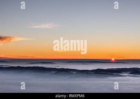 Schönen Sonnenuntergang über einem Tal im Nebel mit Bergen und Hügeln gefüllt Stockfoto