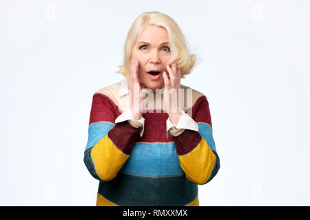 Ältere Frau glücklich und überraschte Ausrufe hält Wangen von Hand. Stockfoto