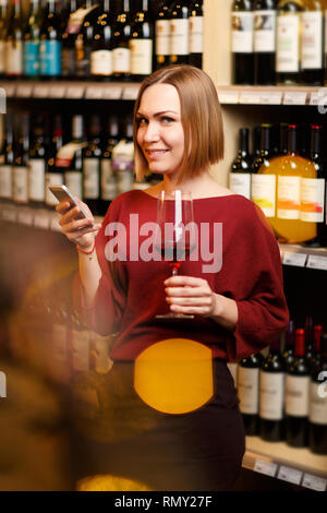 Foto des blonden Jungen mit Glas in der Hand im Geschäft mit Wein Stockfoto