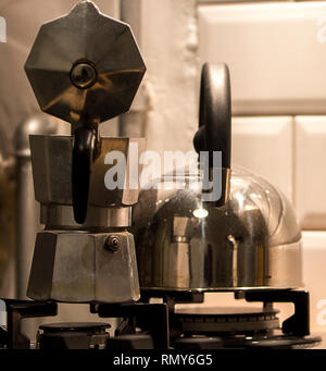 Sephia Nahaufnahme eines Aluminium moka Topf aus Stahl und ein Wasserkocher mit Bakelit Griffe auf einen Gasherd mit weißem Retro keramische Wandfliesen. Stockfoto