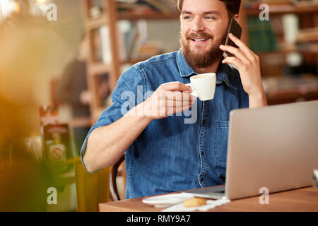 Der moderne Mensch in der Bibliothek Gespräch am Handy und Arbeiten am Laptop Stockfoto