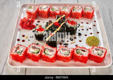 Weiße Platte mit japanischem Sushi rollen, dekoriert mit Mayo, Wasabi und eingelegtem Ingwer. Philadelphia uramaki gefüllt mit Lachs, Gurke, Frischkäse, mit tobiko Roe gedeckt. Stockfoto