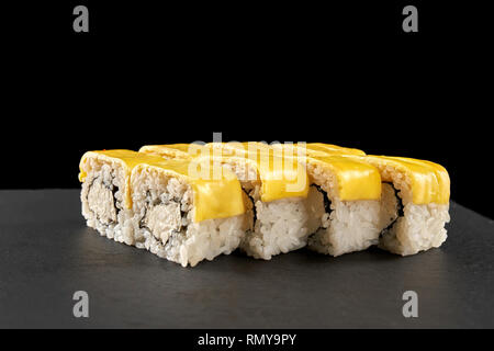 Käse uramaki Sushi Brötchen mit Käse bedeckt. Philadelphia Brötchen gefüllt mit Frischkäse, auf schwarzen Stein Teller serviert. Stockfoto