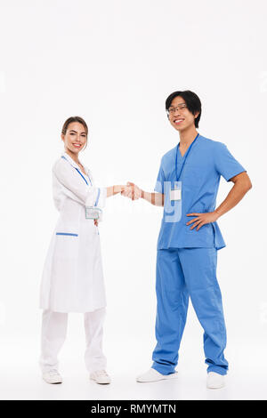 Gerne ärzte Paar tragen Uniform, die auf weißem Hintergrund, Hände schütteln Stockfoto