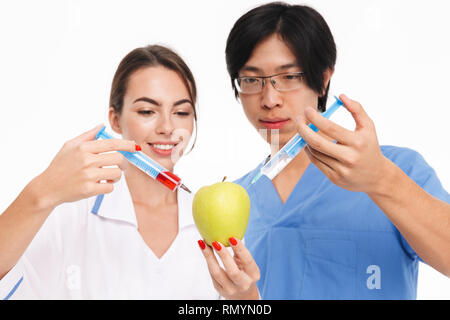 Selbstbewussten jungen multiethnischen Ärzte Paar tragen Uniform, die auf weißem Hintergrund, Flüssigkeit einspritzen in einem Apple Stockfoto