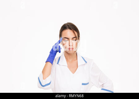 Müde junge Frau Doktor tragen einheitliche und Gummihandschuhe, die auf weißem Hintergrund Stockfoto