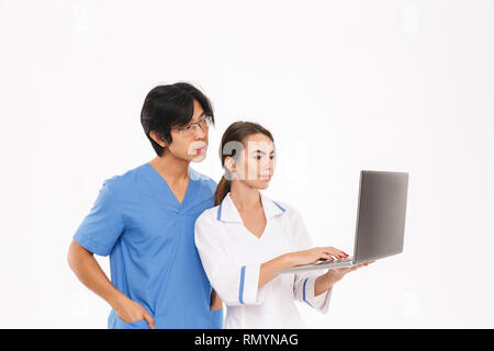 Lächelnd ärzte Paar tragen Uniform, die auf weißem Hintergrund, Arbeiten am Laptop. Stockfoto