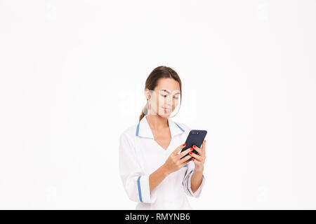 Selbstbewussten jungen Frau Doktor tragen Uniform, die auf weißem Hintergrund, mit Handy Stockfoto