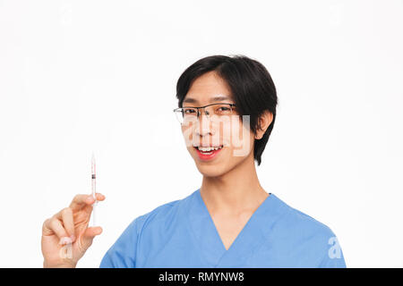 Lächelnd asiatischer Mann Arzt tragen Uniform, die auf weißem Hintergrund, zeigt eine Spritze Stockfoto