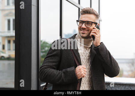Portrait von bärtigen Mann 30 s tragen Brillen zu Fuß durch die Stadt und mit Smartphone Stockfoto