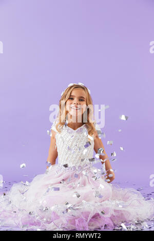 Hübsches kleines Mädchen in Princess Dress über violett Hintergrund sitzen gekleidet Stockfoto