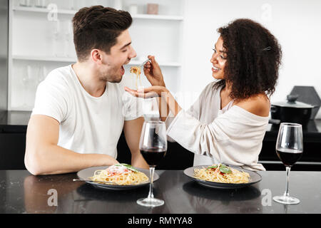 Schönen jungen multiethnischen Paar für ein romantisches Abendessen zu Hause, trinken Rotwein und essen Pasta Stockfoto