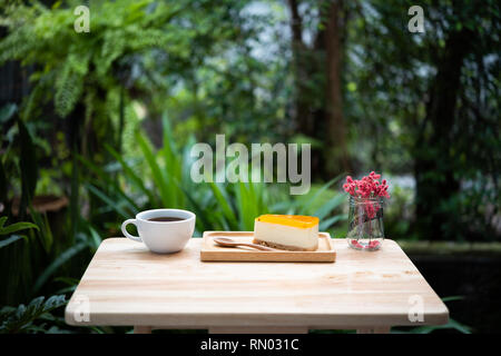 Passion fruit Cheesecake und heißem Kaffee Tasse auf Holz- Fach und Tisch mit grünen Natur Hintergrund Stockfoto