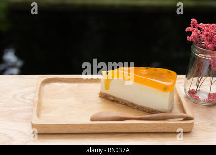 Passion fruit Cheesecake dienen auf Holz Tay und Holztisch mit getrockneten Blumen vase dunklen Hintergrund Stockfoto