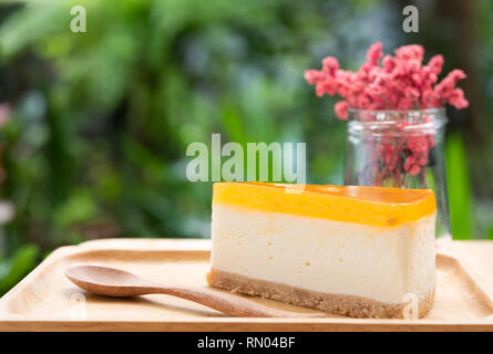 Passion fruit Cheesecake dienen auf Holz Tay und Holztisch mit getrockneten Blumen vase grün Natur Hintergrund Stockfoto