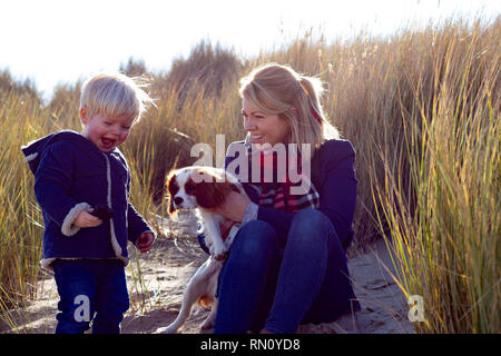 Eine Mutter und Sohn lächelnd Spielen mit Hund im langen Gras Stockfoto