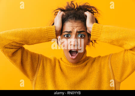 Junge afrikanische Frau mit Pullover, die auf gelben Hintergrund isoliert Schockiert Stockfoto