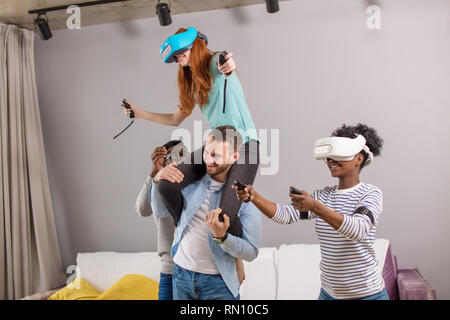 Multiethnische Gruppe von Menschen Spaß und Piggyback ride Frau in VR-Brille zu freudigen Stockfoto