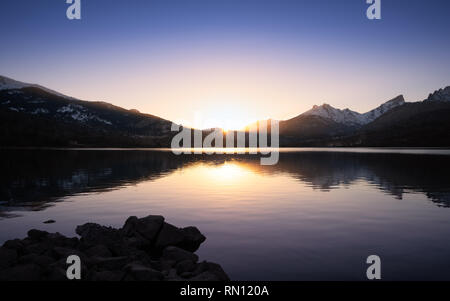 Sonne hinter die schneebedeckten Berge hinter einem ruhigen See Calacuccia in Zentral Korsika Stockfoto