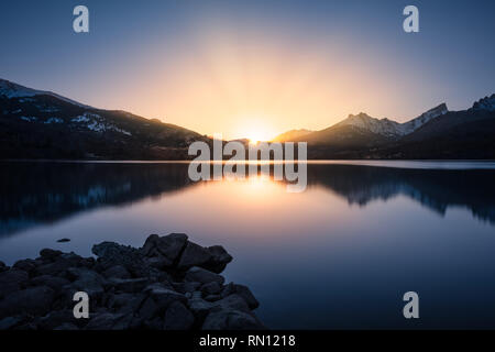 Sonne hinter die schneebedeckten Berge hinter einem ruhigen See Calacuccia in Zentral Korsika Stockfoto