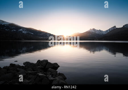 Sonne hinter die schneebedeckten Berge hinter einem ruhigen See Calacuccia in Zentral Korsika Stockfoto