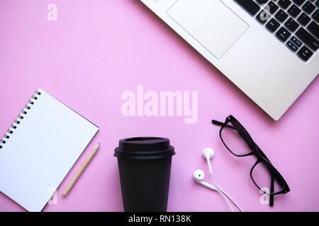 Arbeitsbereich in einem trendigen rosa Farbe. Viele verschiedene Dinge wie einen Laptop und Kopfhörer sind auf dem Tisch. Stockfoto