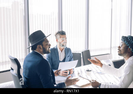 Ernsthafte multi-ethnischen Geschäft Leute am Tisch sitzen, indische Senior Executive im Gespräch mit seinem Nahen Osten und europäischen Partnern, fokussiert Stockfoto