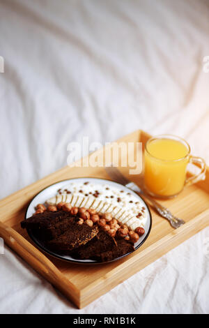 Gesundes Frühstück im Schlafzimmer im Bett Früchte, Nüsse, Stücke Brot und Bananen in einer Platte in ein Fach Stockfoto