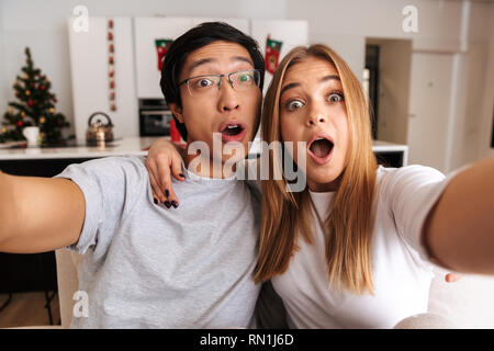Fröhlicher junger Paare auf einer Couch zu Hause zu sitzen, wobei eine selfie Stockfoto