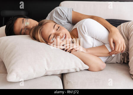 Fröhlicher junger Paar Festlegung auf einer Couch zu Hause, umarmen Stockfoto