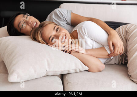 Fröhlicher junger Paar Festlegung auf einer Couch zu Hause, umarmen Stockfoto