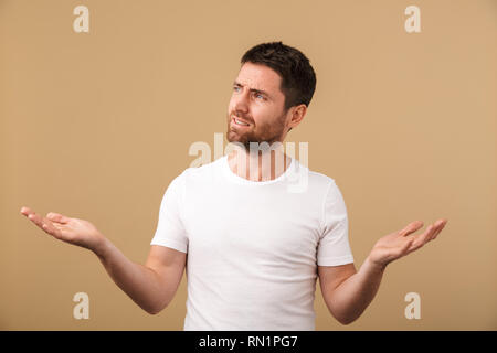 Porträt eines verwirrten jungen Mann beiläufig stehend über beigen Hintergrund isoliert gekleidet Stockfoto
