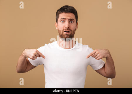 Porträt eines umgekippten junger Mann beiläufig stehend über beige isoliert gekleidet, Pointing Finger auf seine leere t-shirt Stockfoto